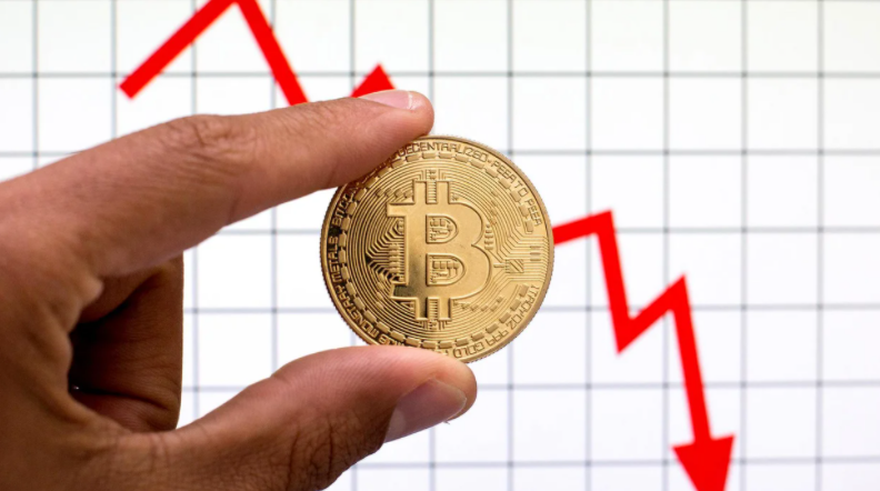 A hand holds a bitcoin against a downward sloping line graph