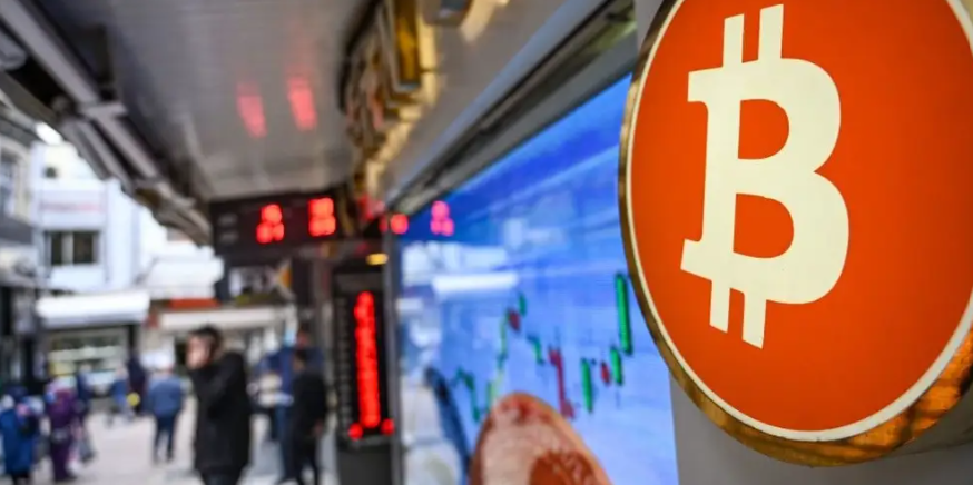 Bitcoin logo sits prominently in the corner inside a trading floor