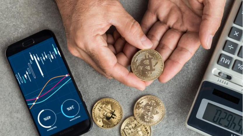 Hands handle several physical bitcoin between a smart phone and a calculator