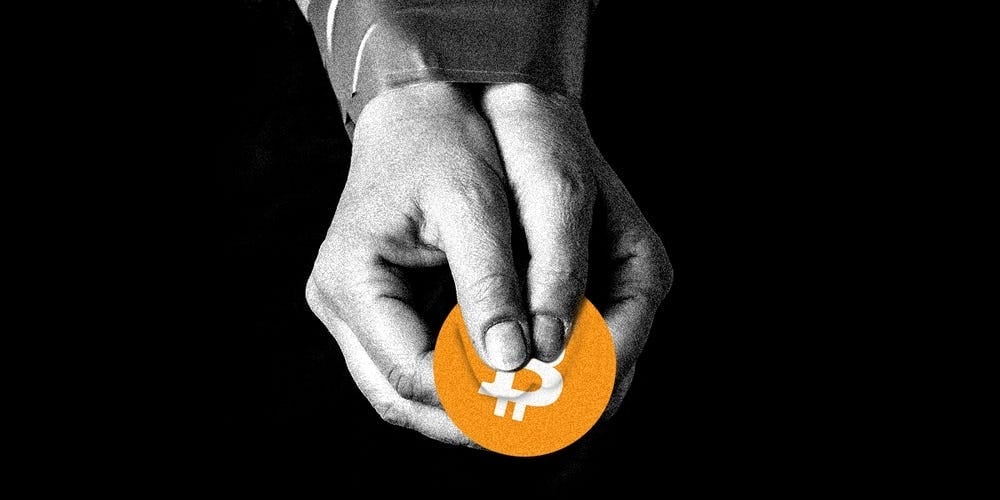 A pair of hands holds a bitcoin against a black background
