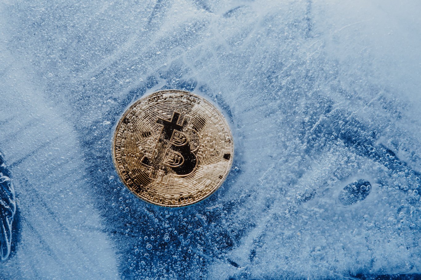 A physical bitcoin sits frozen in a block of ice