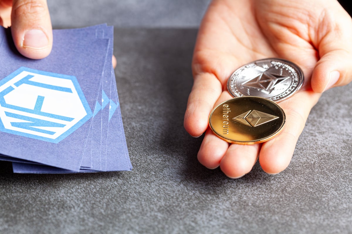 Coins with the Ethereum logo are held next to paper with an NFT emblem