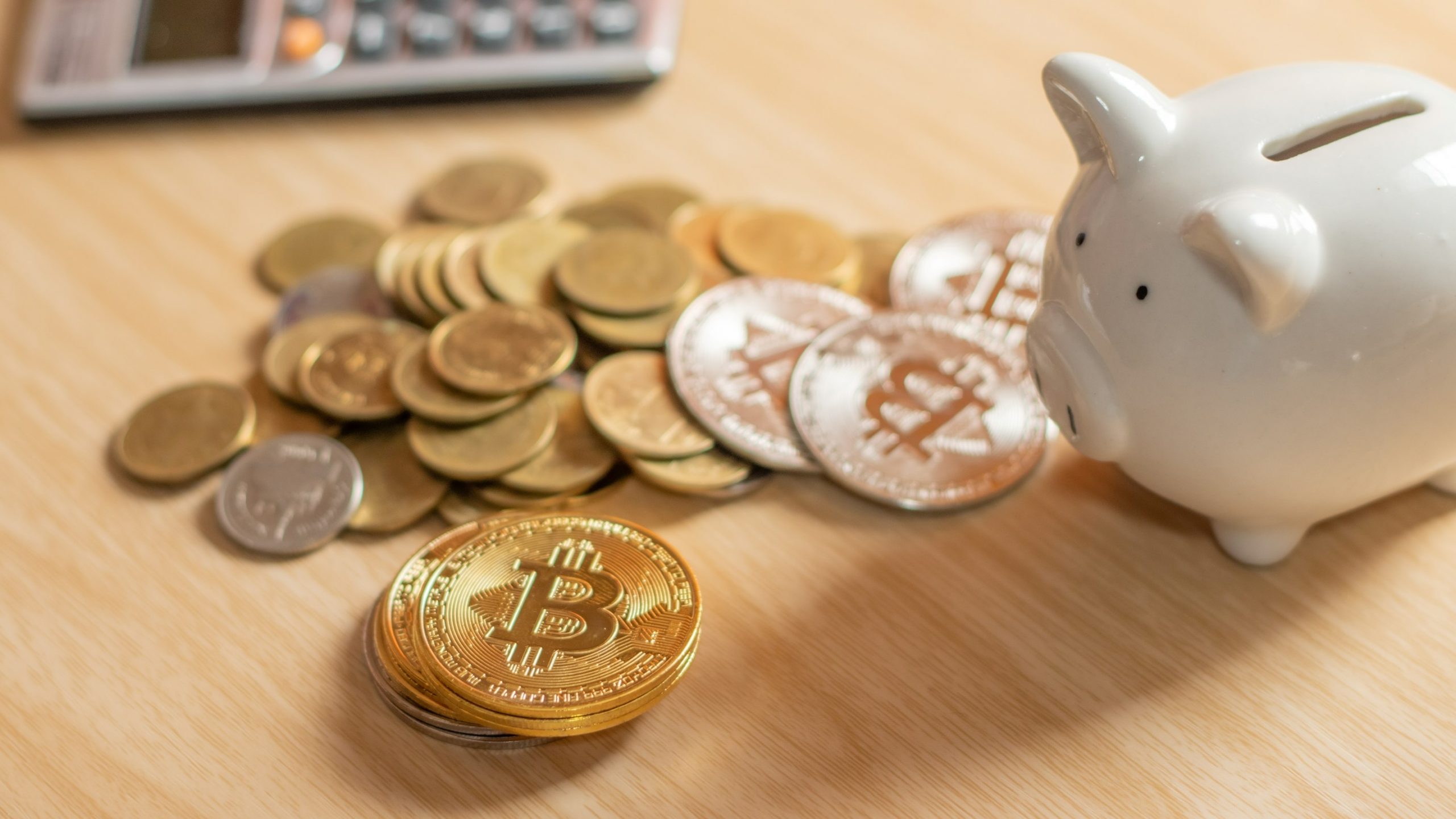 A white piggy bank on a table next to physical bitcoins (Crypto retirement)