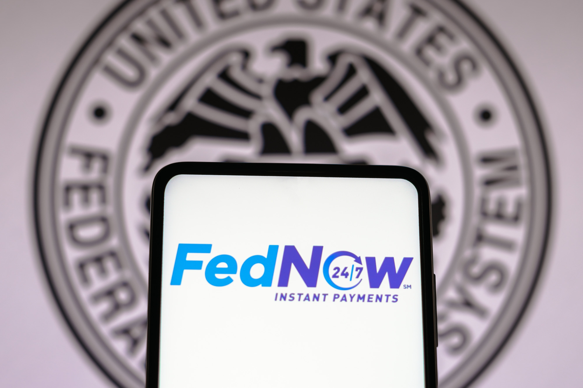 A phone displays the words “FedNow 24/7 Instant Payments” in front of a circle inscribed with an eagle and the words “United States Federal System”